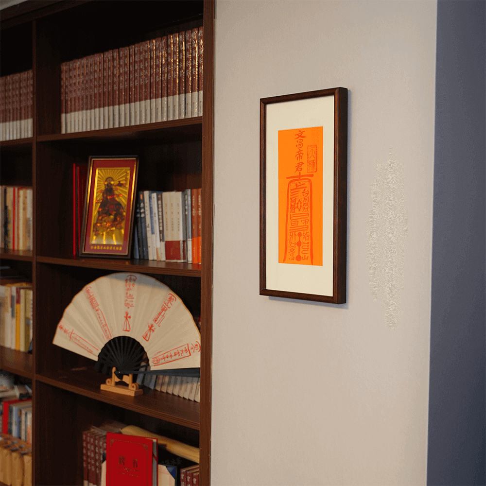 Wenchang Talisman framed artwork hanging on wall above a bookshelf with decorative scholar's objects.