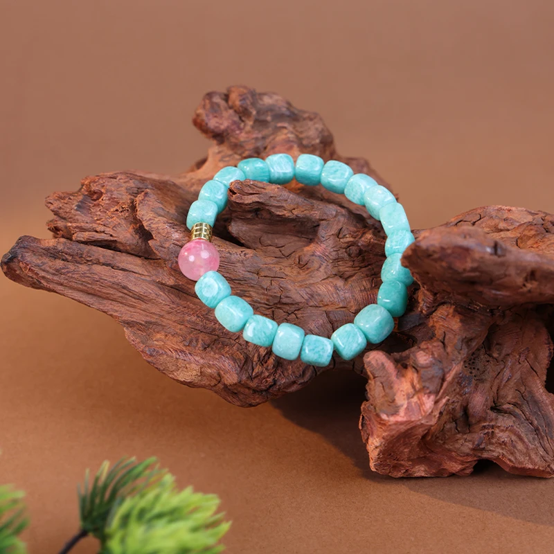 Green amazonite bracelet with a pink blossom bead styled on wood.