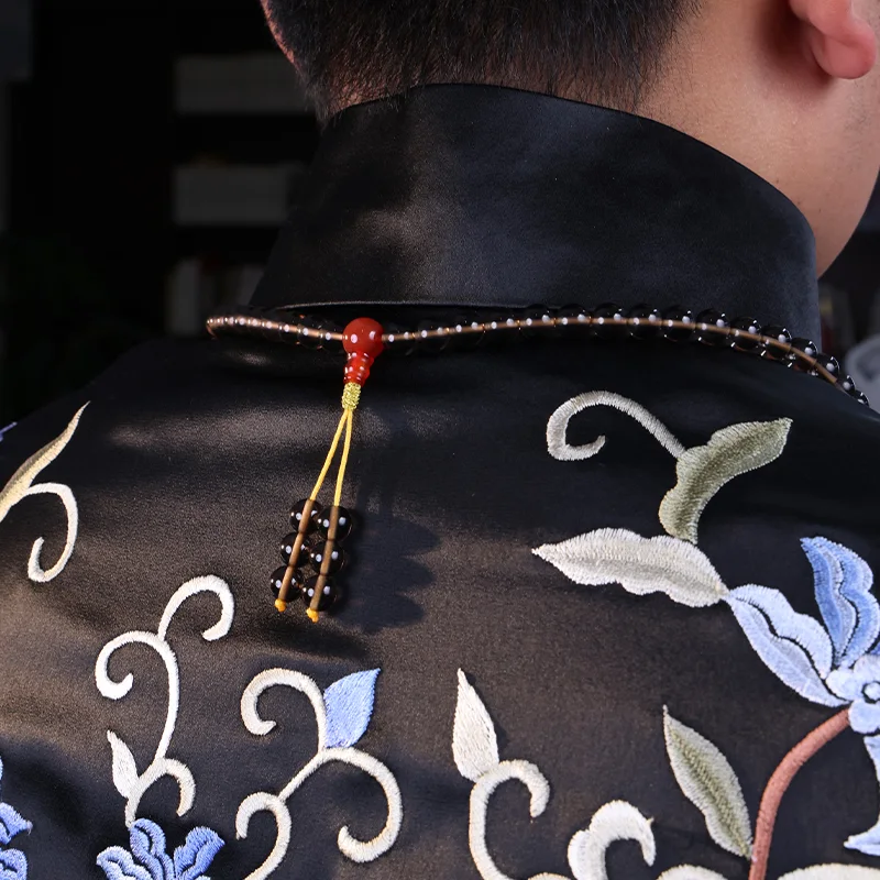 Back detail of an obsidian mala necklace worn on a man's neck.