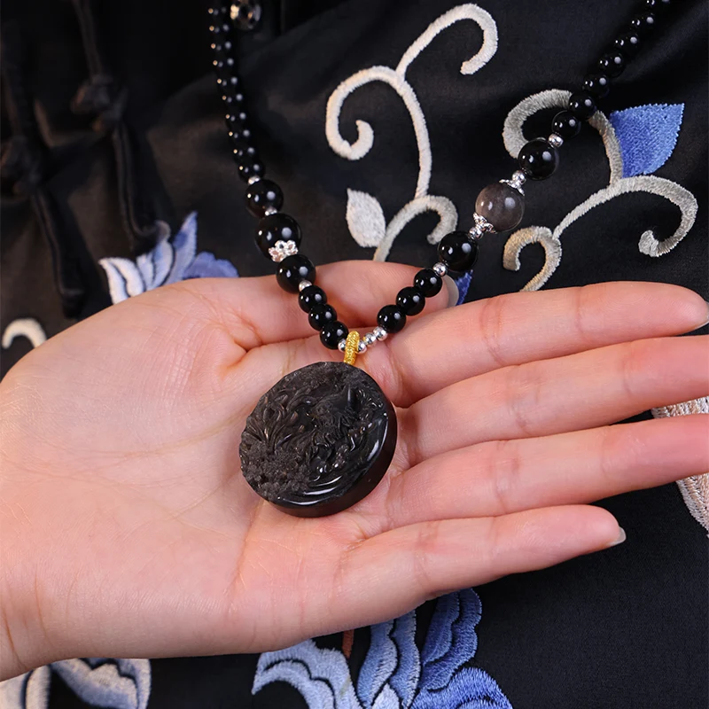 Hand holding a silver obsidian pendant to show intricate carving details.